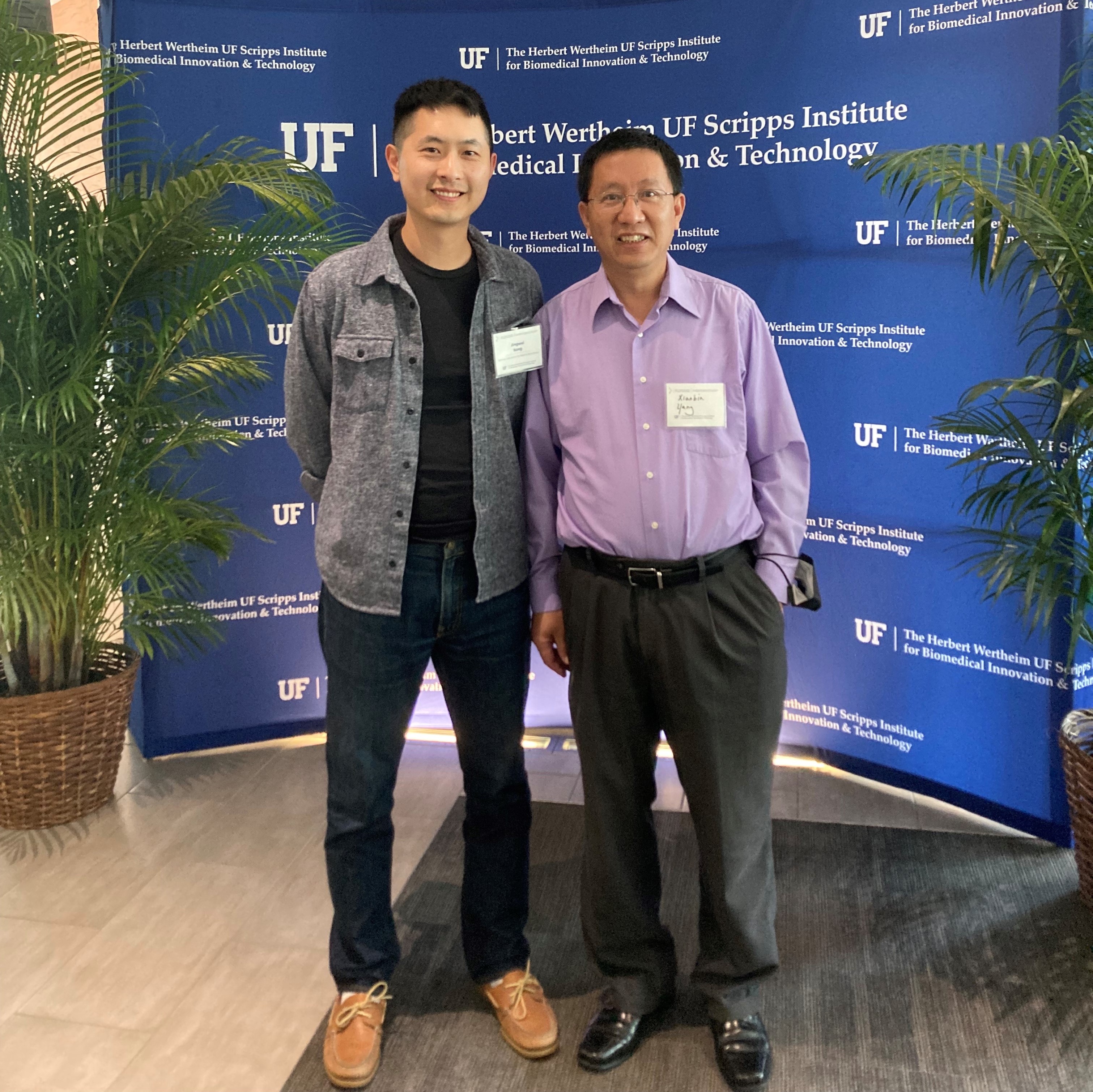 Two men taking a photo behind a backdrop with UF logos