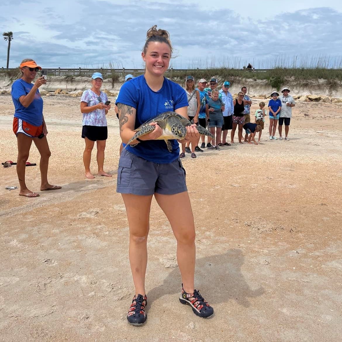 Woman holding sea turtle on beach with crowd getting ready to release the turtle to the ocean