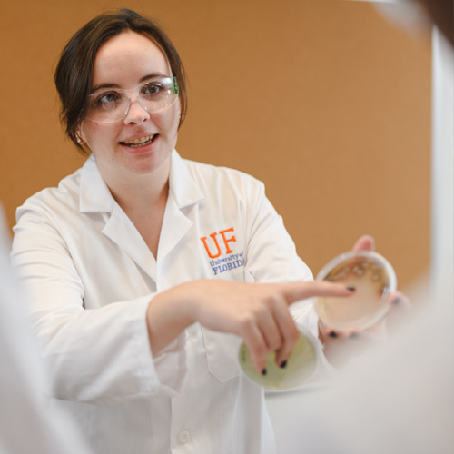 Graduate student in laboratory pointing at petri dish